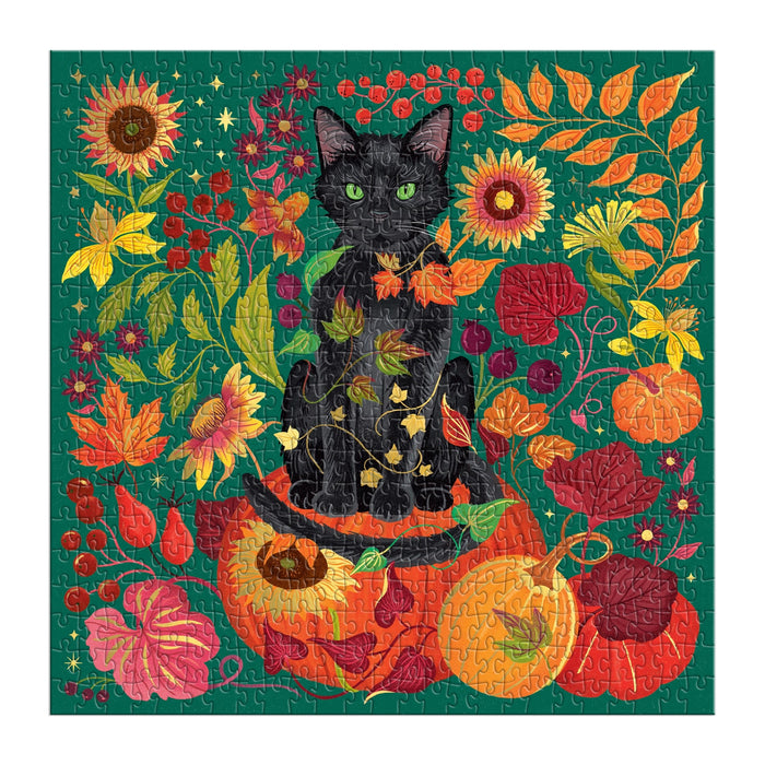 The Whiskers of Autumn 500 Piece Foil Puzzle by Dawn Cooper features a black cat on a carved pumpkin, surrounded by autumn leaves, sunflowers, berries, and pumpkins on a green background—perfect for autumn or Halloween.