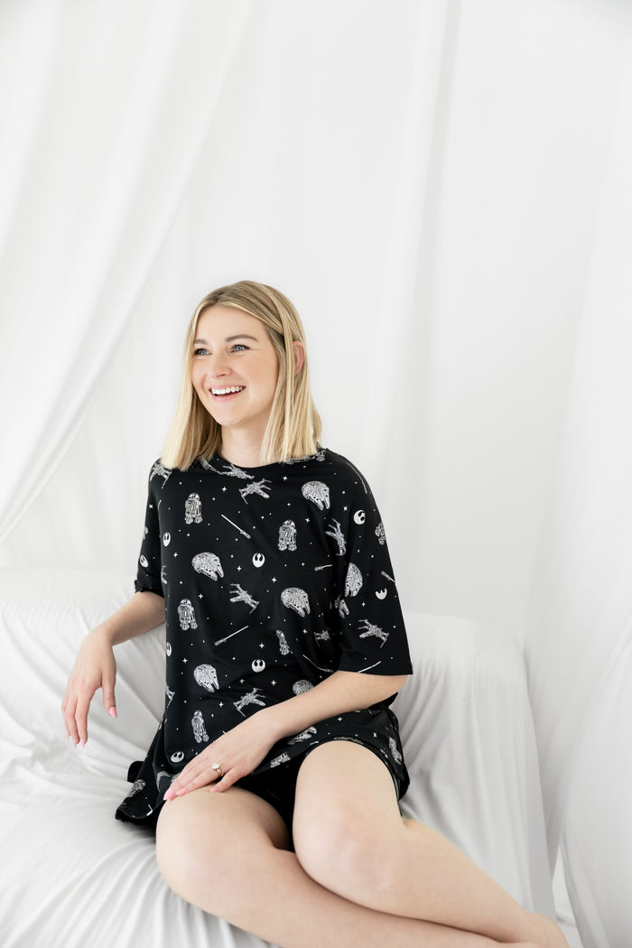 Smiling female sitting in a white blanket wearing the Women’s Biker Short Set in STAR WARS™
