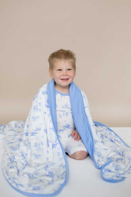 Young boy sitting on his knees with the Youth Blanket in Toile Safari 1.0 around his shoulders