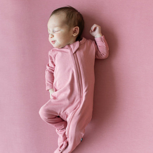Newborn sleeping in Kyte Baby Zippered Footie in Apple Blossom