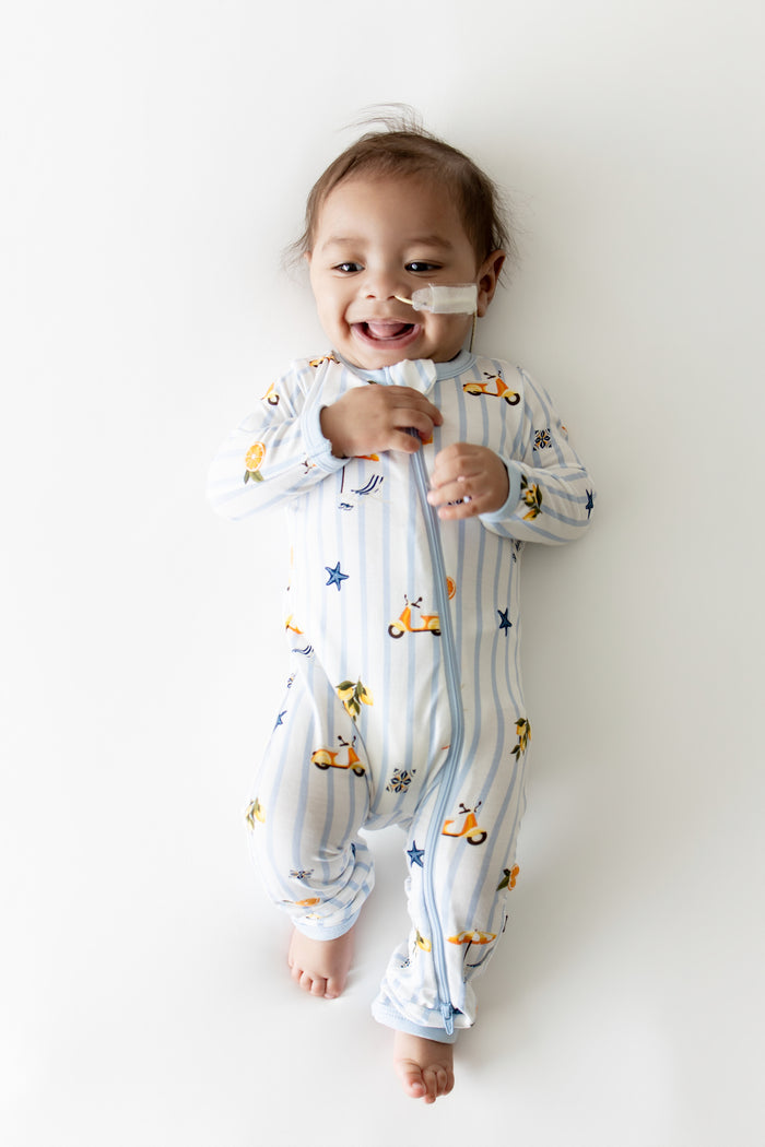 Smiling infant laying on a light surface wearing the Zippered Romper in Amalfi Coast