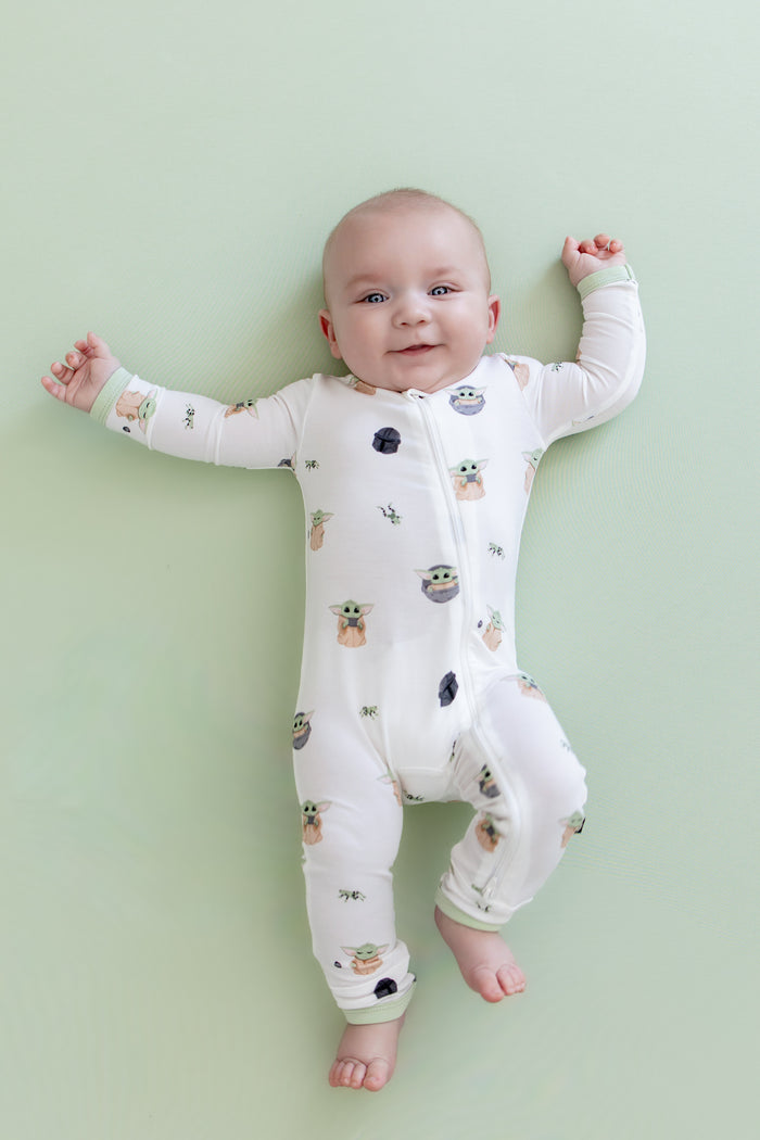 Infant laying on a light green surface wearing the Zippered Romper in Grogu™